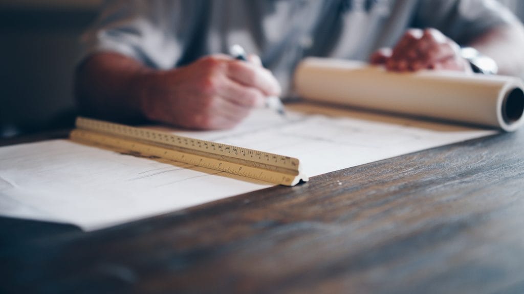 person writing on large sheet of paper and ruler