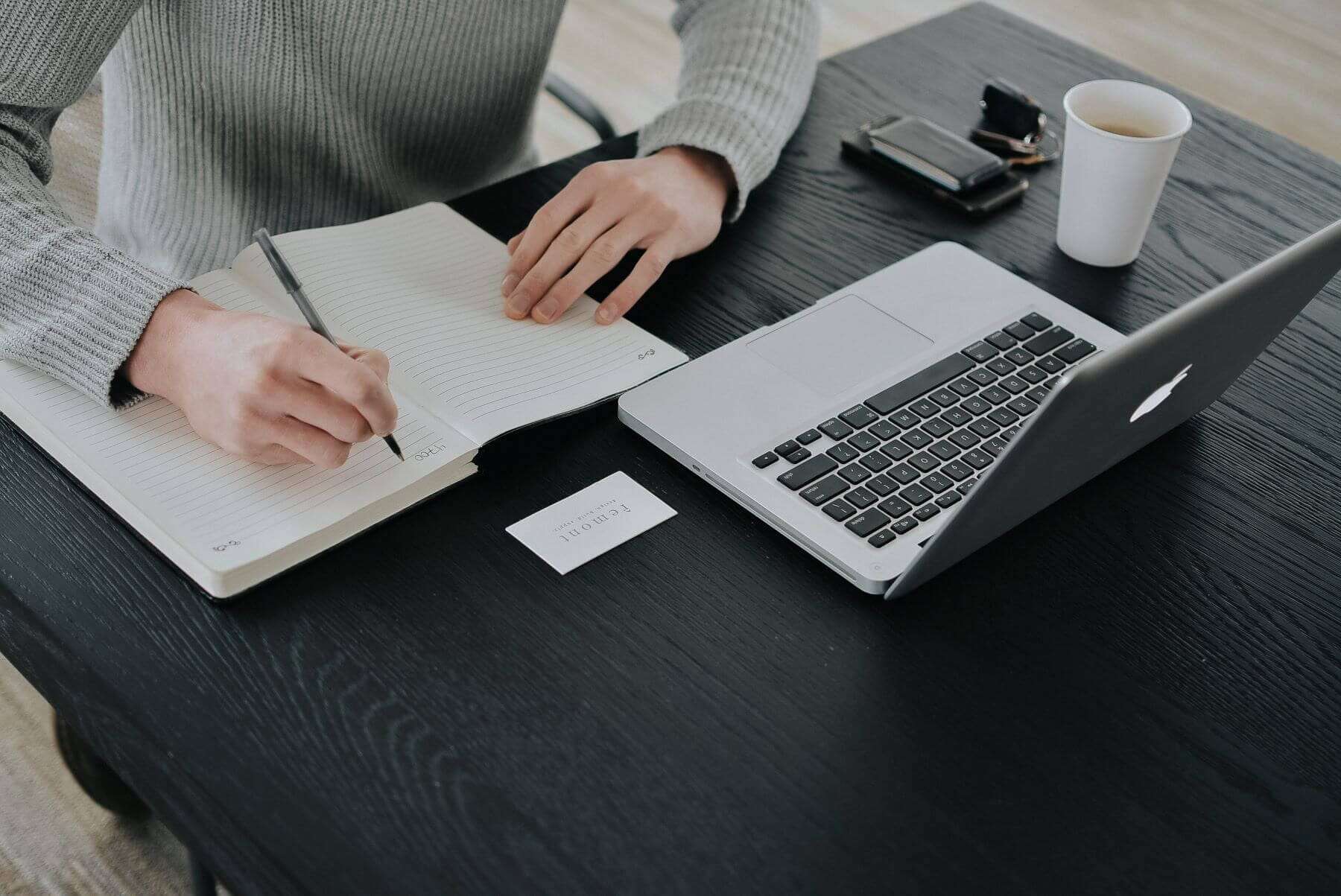 person writing in notebook with laptop at desk